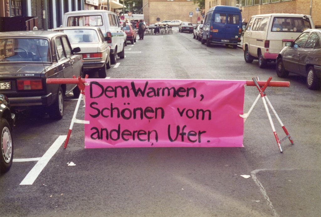 eine Straßenbarrikade in der Klingerstraße mit einem pinkfarbenem Banner, auf dem steht "Dem Warmen Schönen vom anderen Ufer"